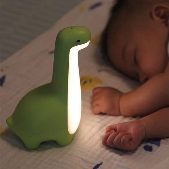 Veilleuse bébé dinosaure verte près d’un nourrisson endormi